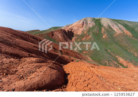 Red clay and green slopes under a blue sky in the mountains Red clay and green slopes under a blue sky in the mountains 125953627