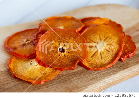 Close up of dried persimmon slices on a wooden cutting board showing detailed texture and star patterns Close up of dried persimmon slices on a wooden cutting board showing detailed texture and star patterns 125953675