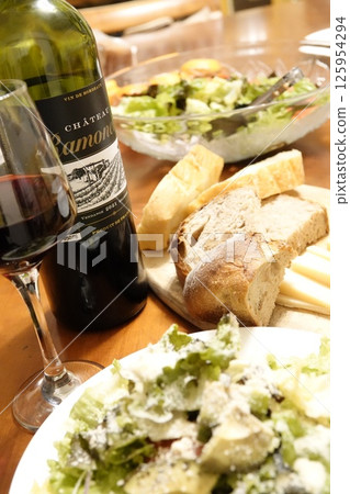 Dinner table with red wine, bread, cheese and salad Dinner table with red wine, bread, cheese and salad 125954294