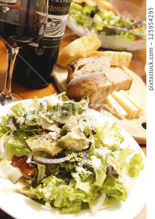 Dinner table with red wine, bread, cheese and salad 125954295