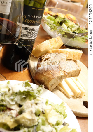 Dinner table with red wine, bread, cheese and salad Dinner table with red wine, bread, cheese and salad 125954296