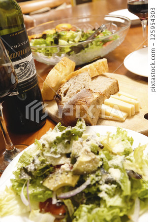 Dinner table with red wine, bread, cheese and salad Dinner table with red wine, bread, cheese and salad 125954303
