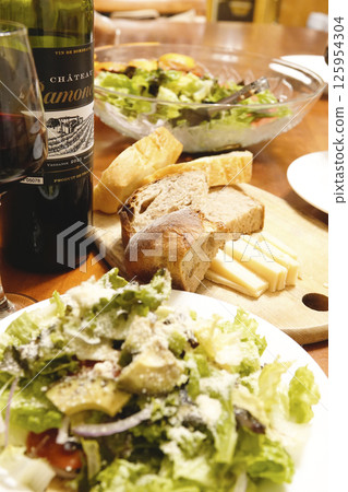 Dinner table with red wine, bread, cheese and salad 125954304