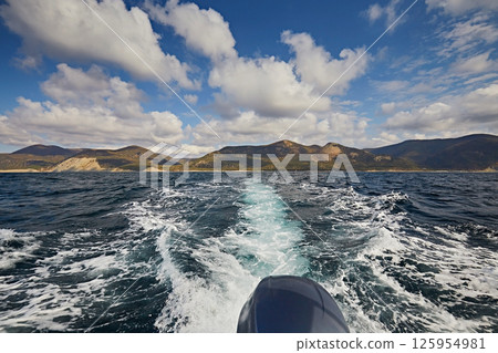 A boat motor trail in the sea and a blue sky with clouds A boat motor trail in the sea and a blue sky with clouds 125954981