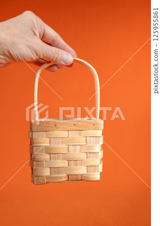 Hand Holds Miniature Woven Basket Against Orange Hand Holds Miniature Woven Basket Against Orange 125955861