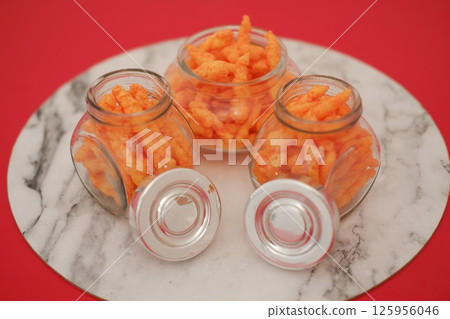 three clear glass jars filled with bright orange cheese-flavored snacks three clear glass jars filled with bright orange cheese-flavored snacks 125956046