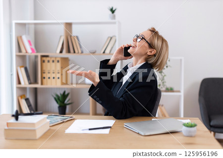 Middle-aged Caucasian woman in business attire talking on phone in modern office workspace 125956196