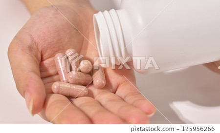 Close-up of capsule-shaped pills falling out of a bottle and lying randomly in a hand. Dietary supplements have the effect of supplementing nutrients. Medical and pharmaceutical treatment concepts. 125956266