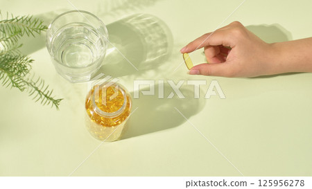 Top view of an open drug bottle, containing hundred golden pills. Each pill is about a finger's length, held carefully between the index finger and thumb. Minimalist layout, medicine concept. Top view of an open drug bottle, containing hundred golden pills. Each pill is about a finger's length, held carefully between the index finger and thumb. Minimalist layout, medicine concept. 125956278