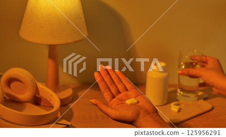 Top view of white pills placed in the palm. The pills are effective in treating headaches and helping patients sleep better. Compact table lamp, body made of natural wood, emits warm yellow light. Top view of white pills placed in the palm. The pills are effective in treating headaches and helping patients sleep better. Compact table lamp, body made of natural wood, emits warm yellow light. 125956291
