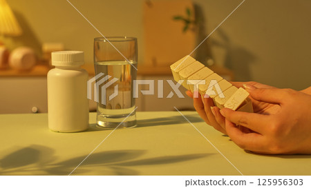 Hands are opening the bottom drawer of the daily medicine jar to take the medicine. A glass of water and a medium sized medicine bottle with a tight lid are placed on the table. Healthcare concept. 125956303
