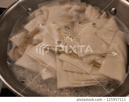 Pasta Beshbarmak sheets softening in rolling boil, revealing translucent layers and culinary transformation within simmering cookware 125957111