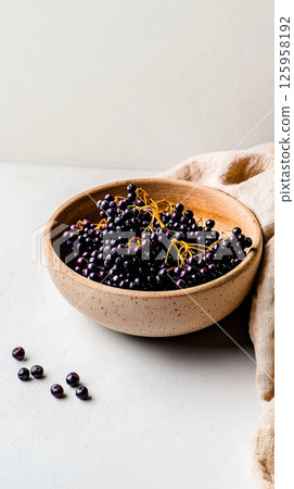 Close-up of plump elderberries in a rustic wooden bowl on a textured surface 125958192