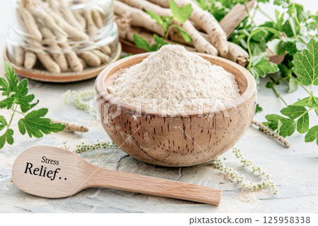 A rustic wooden bowl filled with ashwagandha root powder sits on a weathered table. It is accompanied by fresh herbs and a small wooden spoon labeled with stress relief, creating a calming atmosphere 125958338