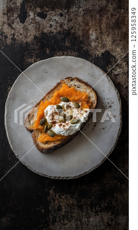 Rustic ceramic plate holding artisan toast spread with ricotta, topped by smooth pumpkin puree, sprinkled with pumpkin seeds and cinnamon against textured surface Rustic ceramic plate holding artisan toast spread with ricotta, topped by smooth pumpkin puree, sprinkled with pumpkin seeds and cinnamon against textured surface 125958349