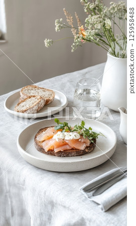 Creamy salmon toast garnished with microgreens beside flowering vase, presenting elegant morning dining experience on rustic wooden surface. Nordic Scandinavian cuisine 125958488
