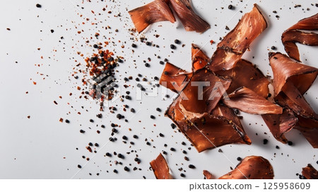 Thin bresaola slices resting on crisp white backdrop, black peppercorns and red chili flakes enhancing rustic italian charcuterie presentation Thin bresaola slices resting on crisp white backdrop, black peppercorns and red chili flakes enhancing rustic italian charcuterie presentation 125958609