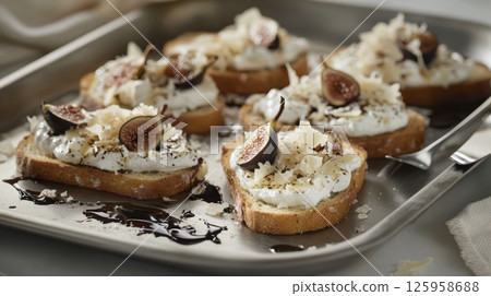 Toasted bread slices spread with cream cheese, crowned with fresh figs, parmesan shavings, and drizzled balsamic glaze on rustic baking sheet 125958688