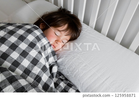 Young caucasian child sleeping peacefully in bed with checkered blanket Young caucasian child sleeping peacefully in bed with checkered blanket 125958871