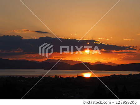 An autumn sunset on the opposite shore of Lake Inawashiro. The sun is reflected on the lake's surface, creating an impressive and beautiful orange sky. An autumn sunset on the opposite shore of Lake Inawashiro. The sun is reflected on the lake's surface, creating an impressive and beautiful orange sky. 125959206