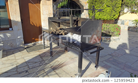 A retro barbecue stands ready in the courtyard of a small restaurant, filled with ash and firewood. The outdoor space hints at a cozy atmosphere perfect for grilling and enjoying meals. A retro barbecue stands ready in the courtyard of a small restaurant, filled with ash and firewood. The outdoor space hints at a cozy atmosphere perfect for grilling and enjoying meals. 125959423
