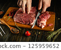 Hands skillfully cut raw meat on a wooden board surrounded by fresh spices and herbs, creating an inviting atmosphere in a traditional kitchen 125959652