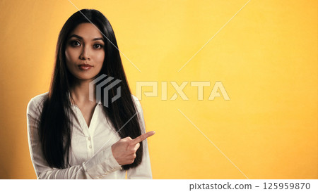 Young Asian businesswoman pointing finger to the right on yellow background Young Asian businesswoman pointing finger to the right on yellow background 125959870