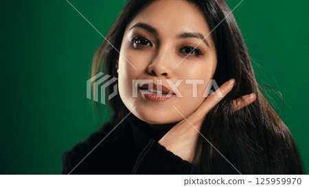 Beautiful asian woman touching her hair on green background Beautiful asian woman touching her hair on green background 125959970