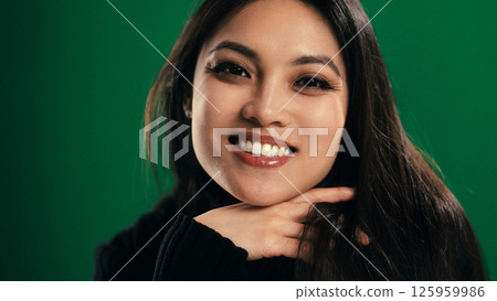Smiling asian woman posing with hand on chin on green background 125959986