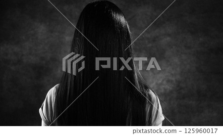 Woman with long black hair hiding her face in studio shot Woman with long black hair hiding her face in studio shot 125960017