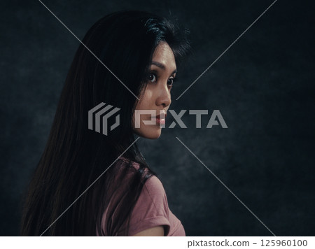 Young woman with long black hair turning head and looking over shoulder Young woman with long black hair turning head and looking over shoulder 125960100