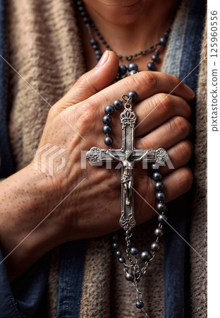 A CloseUp Image of a Hand Gracefully Holding a Silver Cross Alongside Rosary Beads 125960556