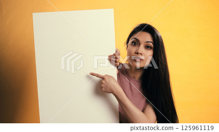 Young asian woman pointing at blank board on yellow background 125961119