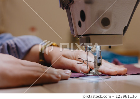 woman sews piece of cloth on sewing machine. industrial metal machine for all fabric tops.  125961130