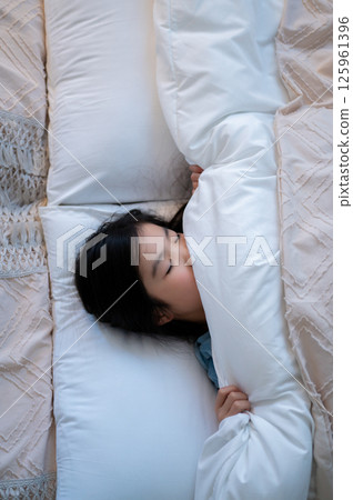The girl's peaceful sleeping face, wrapped in a white pillow and futon, is striking. 125961396