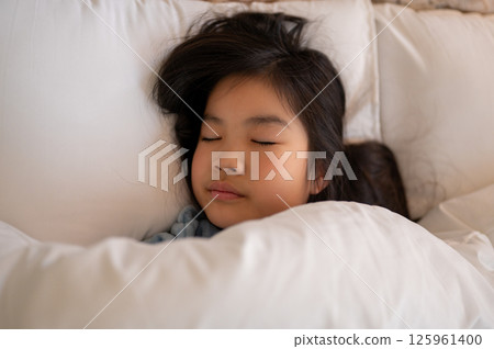 一個女孩在臥室裡裹著被褥安靜地睡覺，周圍環繞著柔和的燈光 125961400