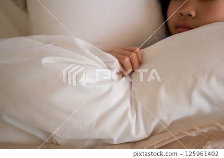 The innocent sleeping figure of a girl hugging a white futon tightly 125961402