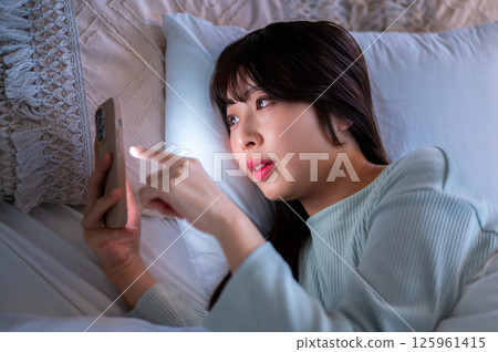 A woman lying in bed looking at her smartphone and moving her fingers 125961415