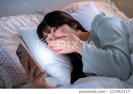 A woman yawning while looking at her smartphone A woman yawning while looking at her smartphone 125961417