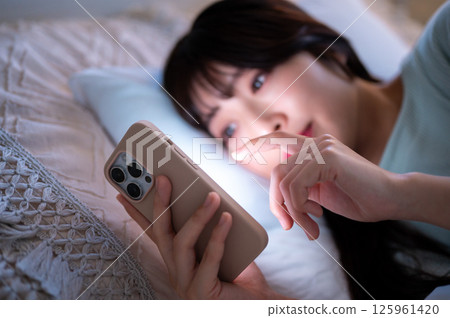 A woman scrolling through her smartphone screen in a dark bedroom A woman scrolling through her smartphone screen in a dark bedroom 125961420