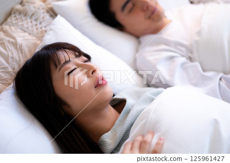 A warm relationship between a woman who has her eyes closed in bed and a man who is quietly watching over her 125961427