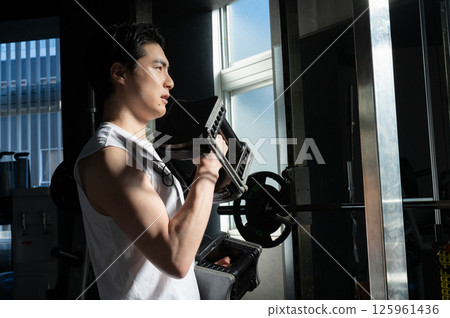 A man lifting dumbbells at the gym, concentrating on training with a serious expression A man lifting dumbbells at the gym, concentrating on training with a serious expression 125961436