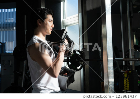 A gym scene where a man exercising with a barbell stands out in a powerful manner A gym scene where a man exercising with a barbell stands out in a powerful manner 125961437