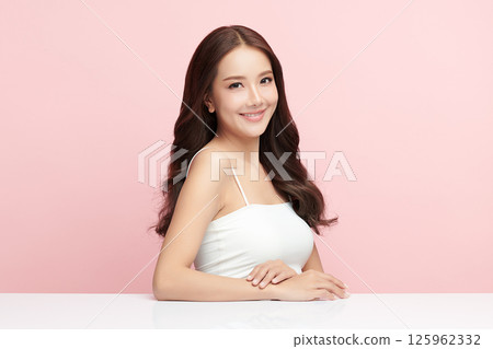 A beautiful young Asian woman with clean, fresh skin against a pink background. Skincare, facial treatment, cosmetology, beauty, and spa. An elegant portrait of an Asian woman. 125962332