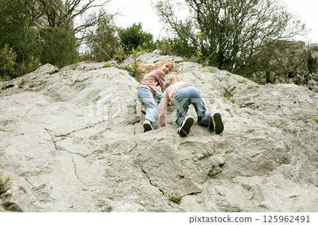 two little girls sisters twins climbing on rock together outside 125962491