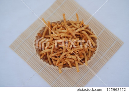 a round wicker basket filled with crunchy, fried stick-shaped snacks 125962552