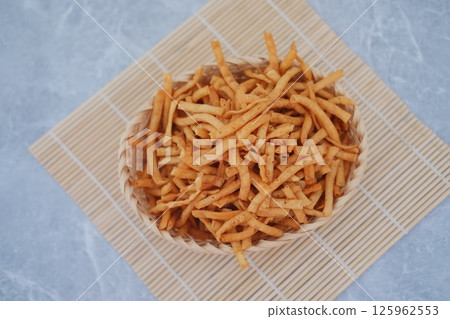 a round wicker basket filled with crunchy, fried stick-shaped snacks 125962553