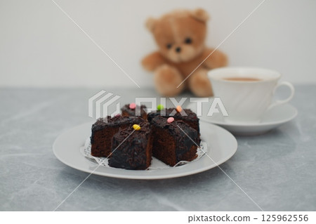 a plate of chocolate cake slices topped with glossy chocolate glaze, chocolate sprinkles, and colorful candy pieces 125962556