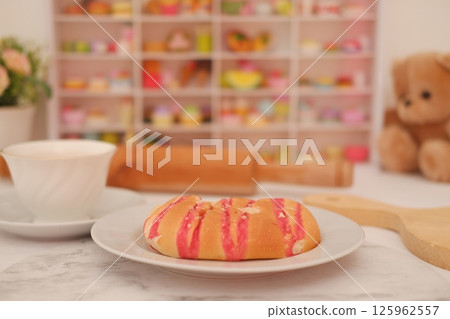 a soft bread roll topped with vibrant pink icing stripes and crushed nuts, served on a white plate 125962557