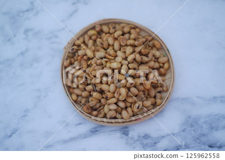 a round bamboo tray filled with roasted soybeans placed on a light marble surface 125962558